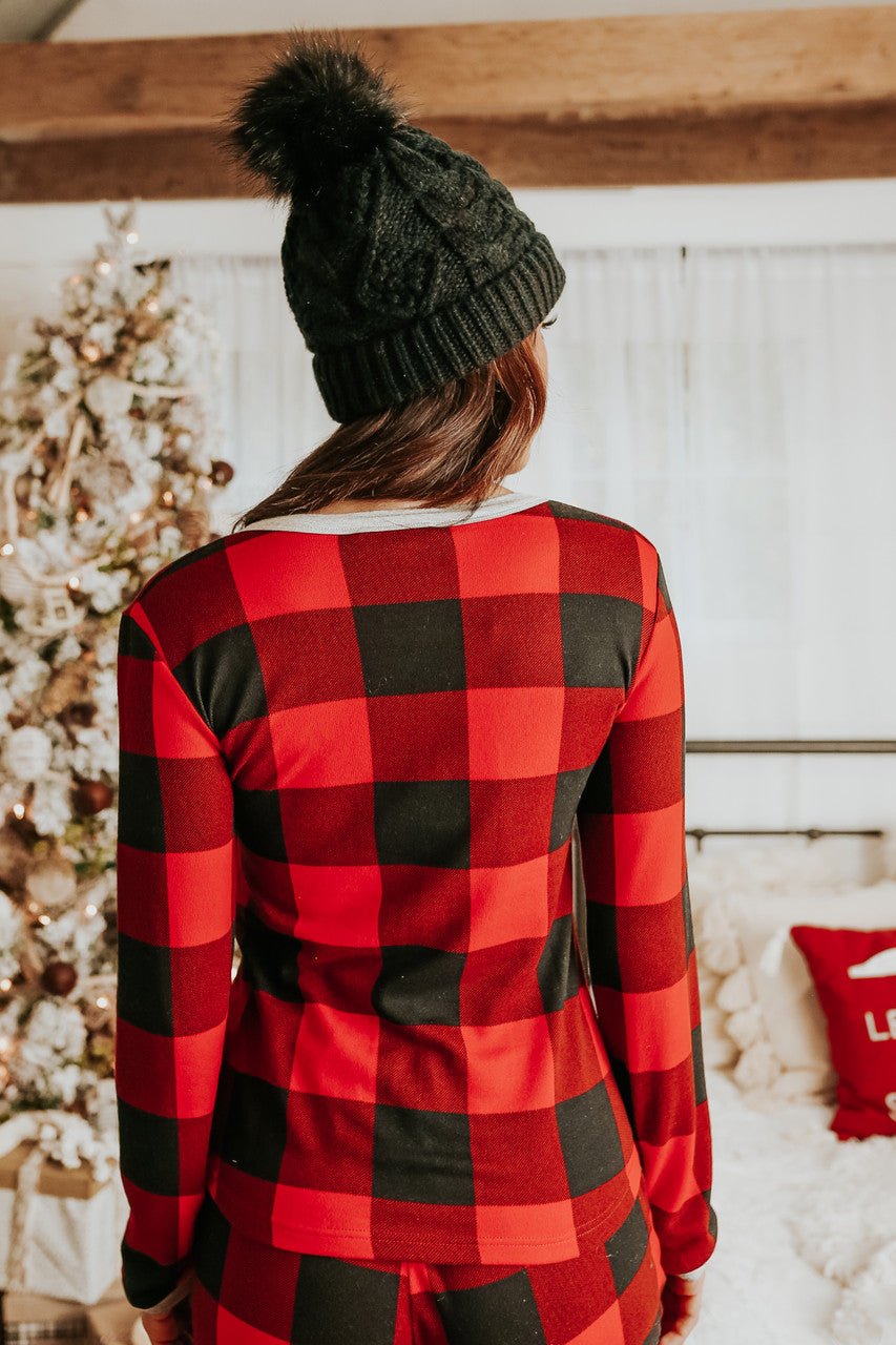 A person in a Christmas Morning Red Plaid Pajama Set stands by a brightly decorated indoor Christmas tree, facing away.