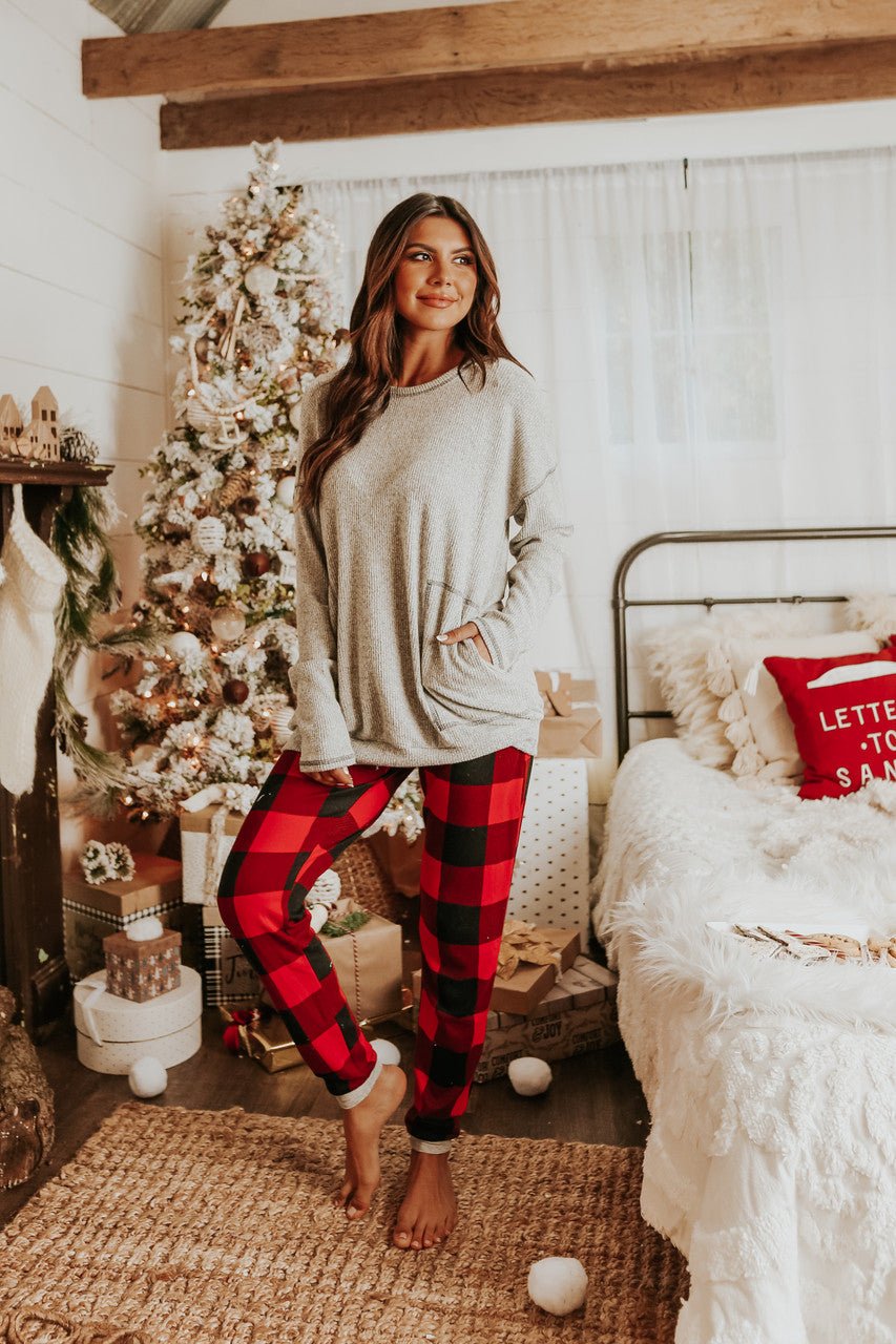 Woman wears the Christmas Morning Red Plaid Pajama Set, standing by a decorated Christmas tree in a cozy, festive bedroom.