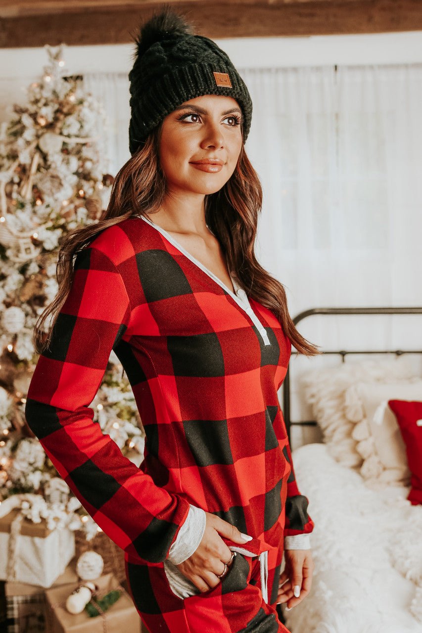 Woman in the Christmas Morning Red Plaid Pajama Set stands by a Christmas tree in a festive bedroom.