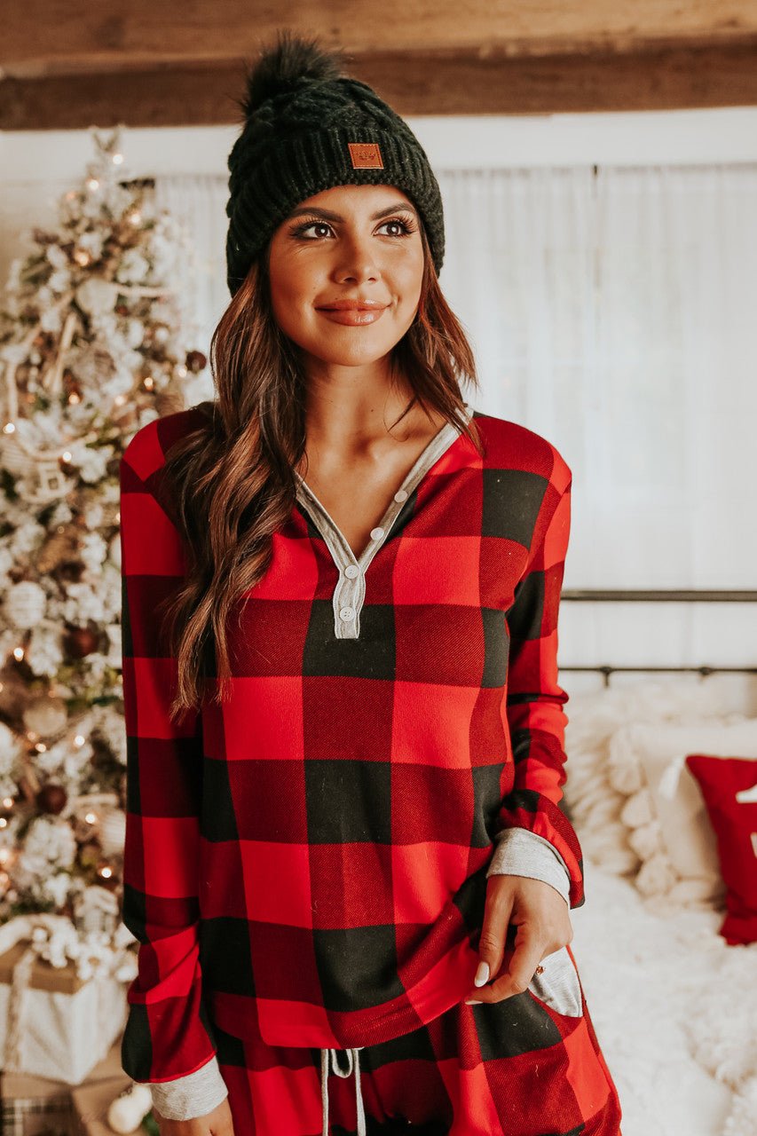 A woman in the Christmas Morning Red Plaid Pajama Set stands indoors by a decorated Christmas tree.