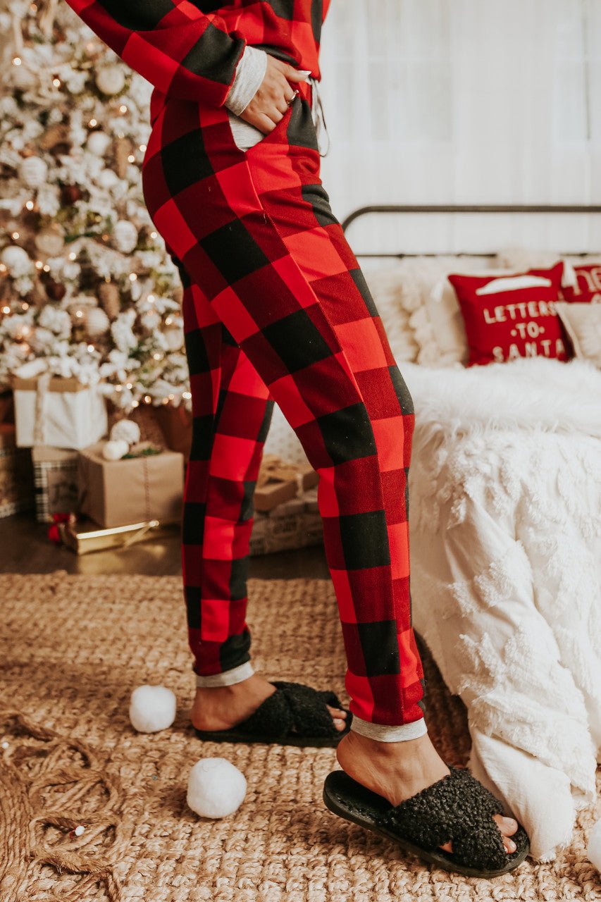 Person in the Christmas Morning Red Plaid Pajama Set stands by a Christmas tree and gifts in a cozy, festive living room.
