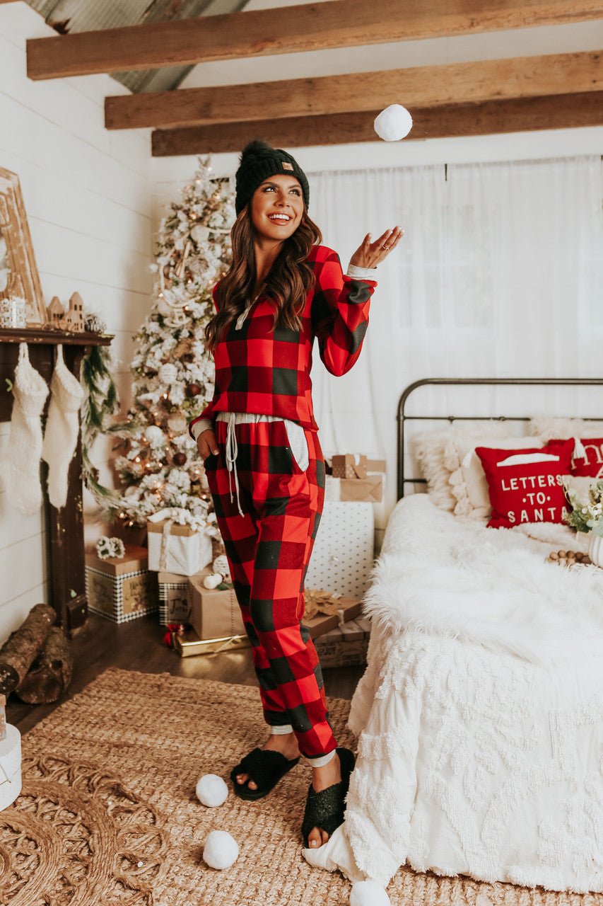 A woman in the Christmas Morning Red Plaid Pajama Set tosses a snowball in a cozy, festive, Christmas-decorated room.