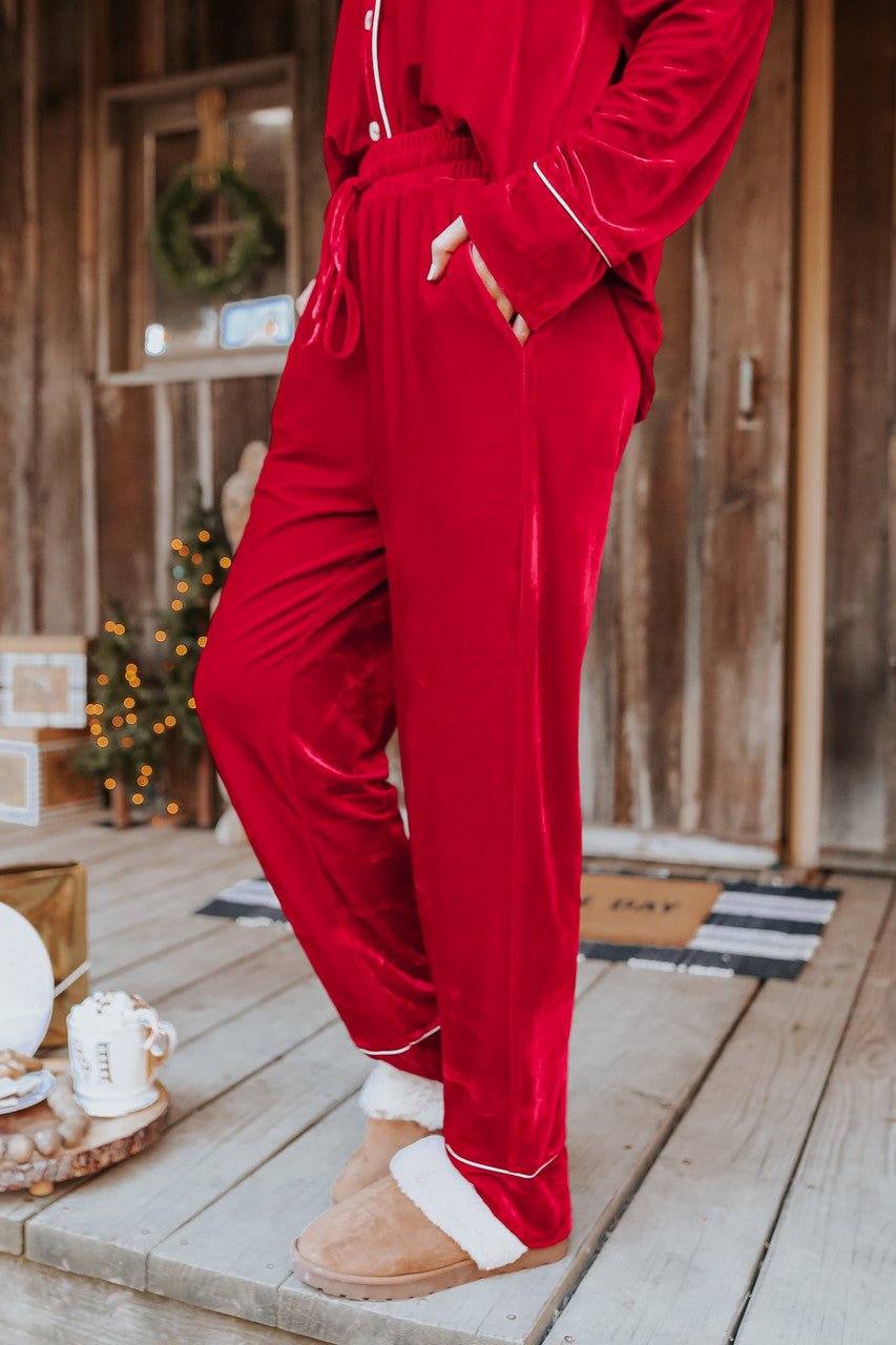 Someone in a North Pole Burgundy Velvet Pajama Set stands on a Christmas porch with gifts and festive holiday decor in the background.