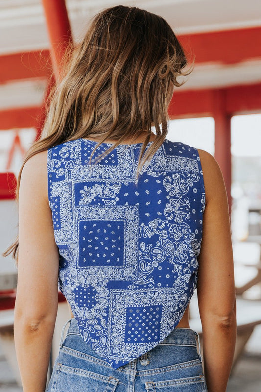 Woman with wavy hair wears the Out West Blue Bandana Print Sleeveless Cowl Neck Top and jeans, photographed from behind.