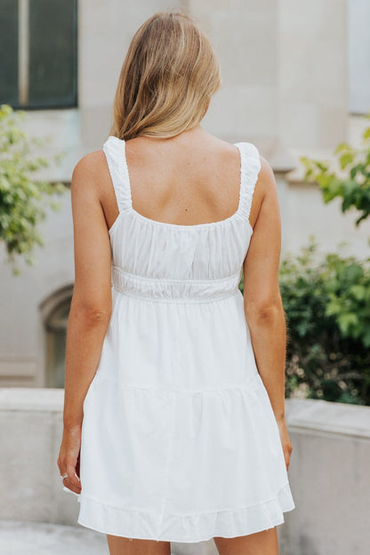 A blonde woman wears the Square Neck White Gathered Tiered Dress - FINAL SALE, standing outdoors with her back to the camera.