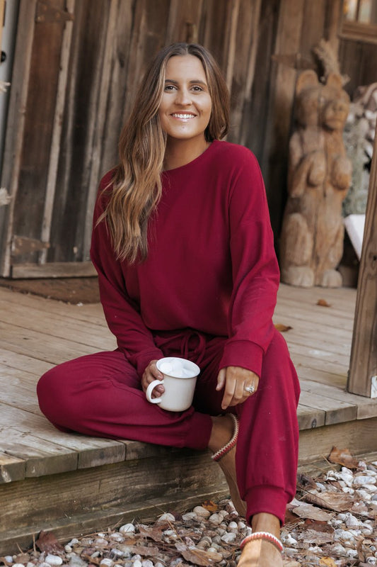 Woman in the Step Up Lounge Set sits on a wooden porch, smiling with a white mug, rustic decor in the background.