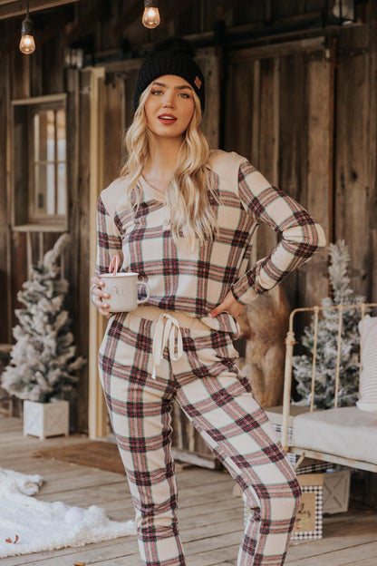 Woman in a black beanie and Taupe Tartan Plaid Jogger Pajama Pants - FINAL SALE stands on a snowy porch with festive holiday décor.
