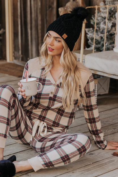A woman in Taupe Tartan Plaid Jogger Pajama Pants sits on a wooden porch, holding a mug and looking to the side.