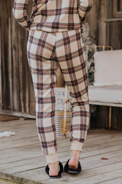 A person in Taupe Tartan Plaid Jogger Pajama Pants - FINAL SALE and black slippers stands on a wooden porch, seen from behind.